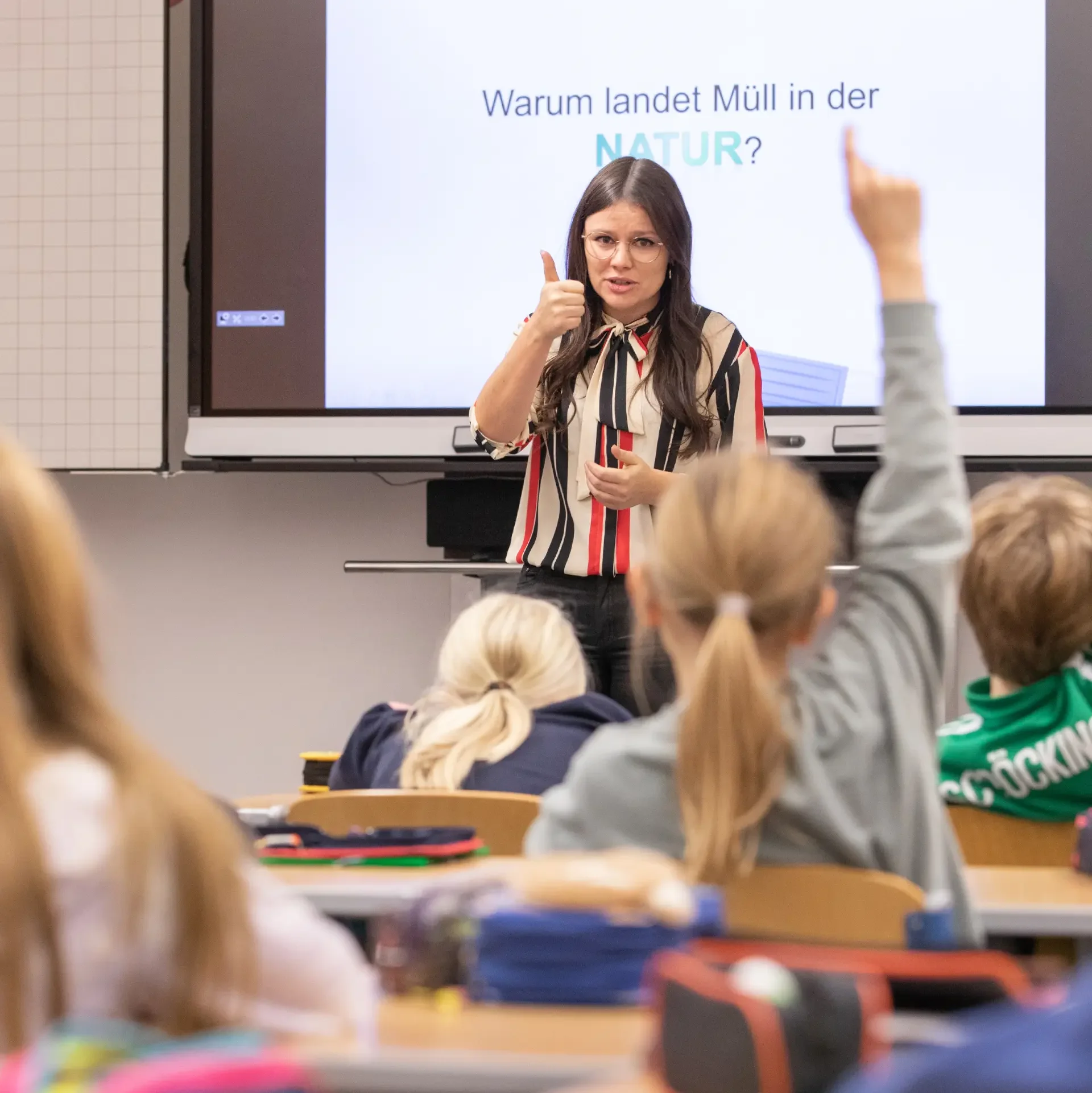 Frau erklärt einer etwas Schulklasse, Kind meldet sich