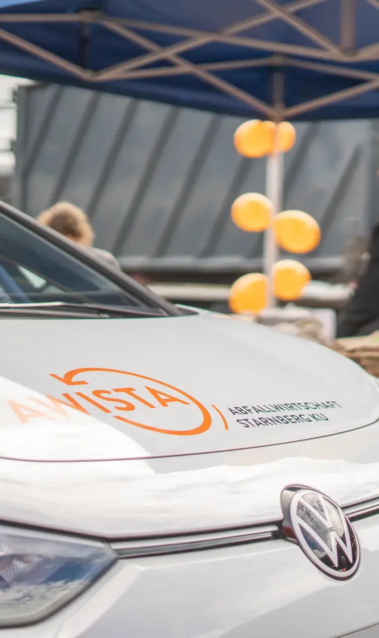 Fahrzeug von AWISTA-Starnberg mit Logo auf der Motorhaube vor einem Pavillon mit orangenen Ballons